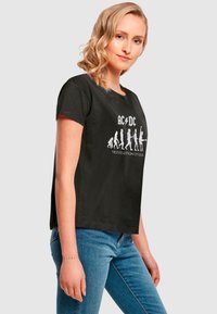 Schwarz Baumwoll-T-Shirt mit Rundhalsausschnitt und kurzen Ärmeln. Mit einem weißen Grafikdruck, der "Die Evolution des Rocks" mit Figuren darstellt.