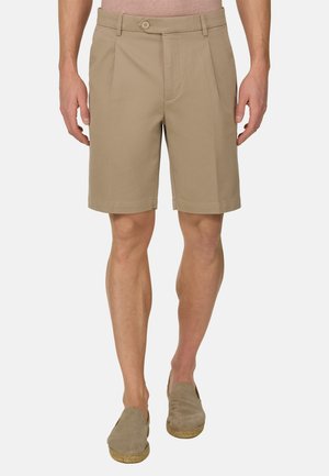 Homme portant un short beige ajusté jusqu'au genou et des espadrilles assorties, debout devant un fond clair uni.