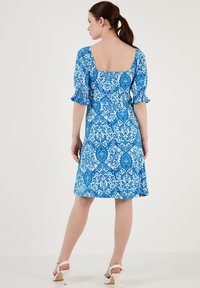 Rochie bleu cu un decolteu pătrat, mâneci scurte voluminoase și o siluetă în A. Materialul are modele florale și geometrice intricate.