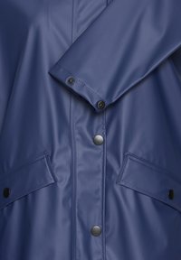 Impermeabile blu navy realizzato in nylon liscio, dotato di bottoni a pressione neri e due tasche frontali con pattina.