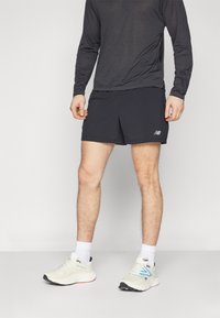Calções desportivos pretos com um logótipo na perna esquerda, combinados com uma camisa de manga comprida cinza escuro e sapatilhas brancas.