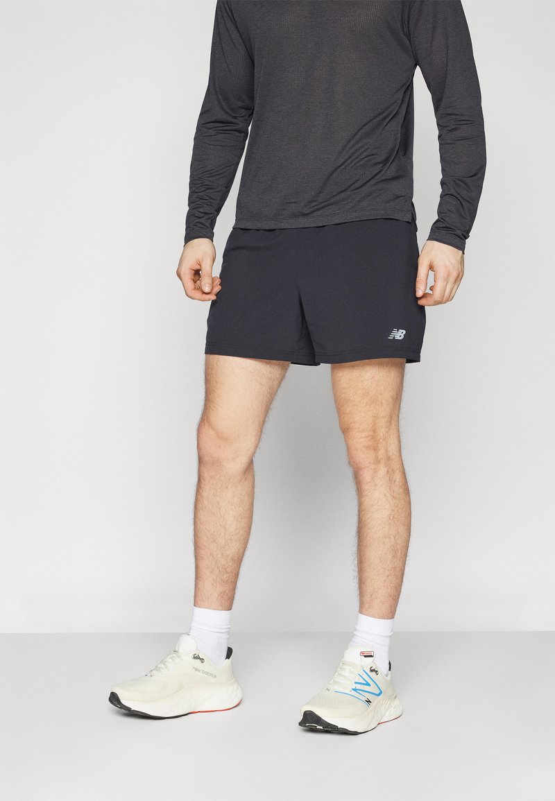Calções desportivos pretos com um logótipo na perna esquerda, combinados com uma camisa de manga comprida cinza escuro e sapatilhas brancas.