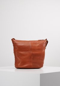 Hnědá kožená kabelka s jednoduchým, strukturovaným designem, se zipovým uzávěrem a bočními švy, umístěná na neutrálním pozadí.