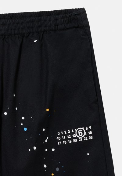 Μαύρο ύφασμα με ελαστική μέση, διασκορπισμένες λευκές, μπλε και κίτρινες βαφές, και λευκοί αριθμοί 0-23 με τον αριθμό 6 κυκλωμένο στη δεξιά πλευρά.