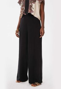 Zwarte wijde broek van lichtgewicht stof, gecombineerd met een cropped, gemusterde blouse met korte mouwen en decoratieve accenten.