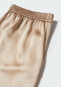 Joggers beige de satén con cintura elástica y textura suave, que muestran un corte relajado y un sutil brillo.