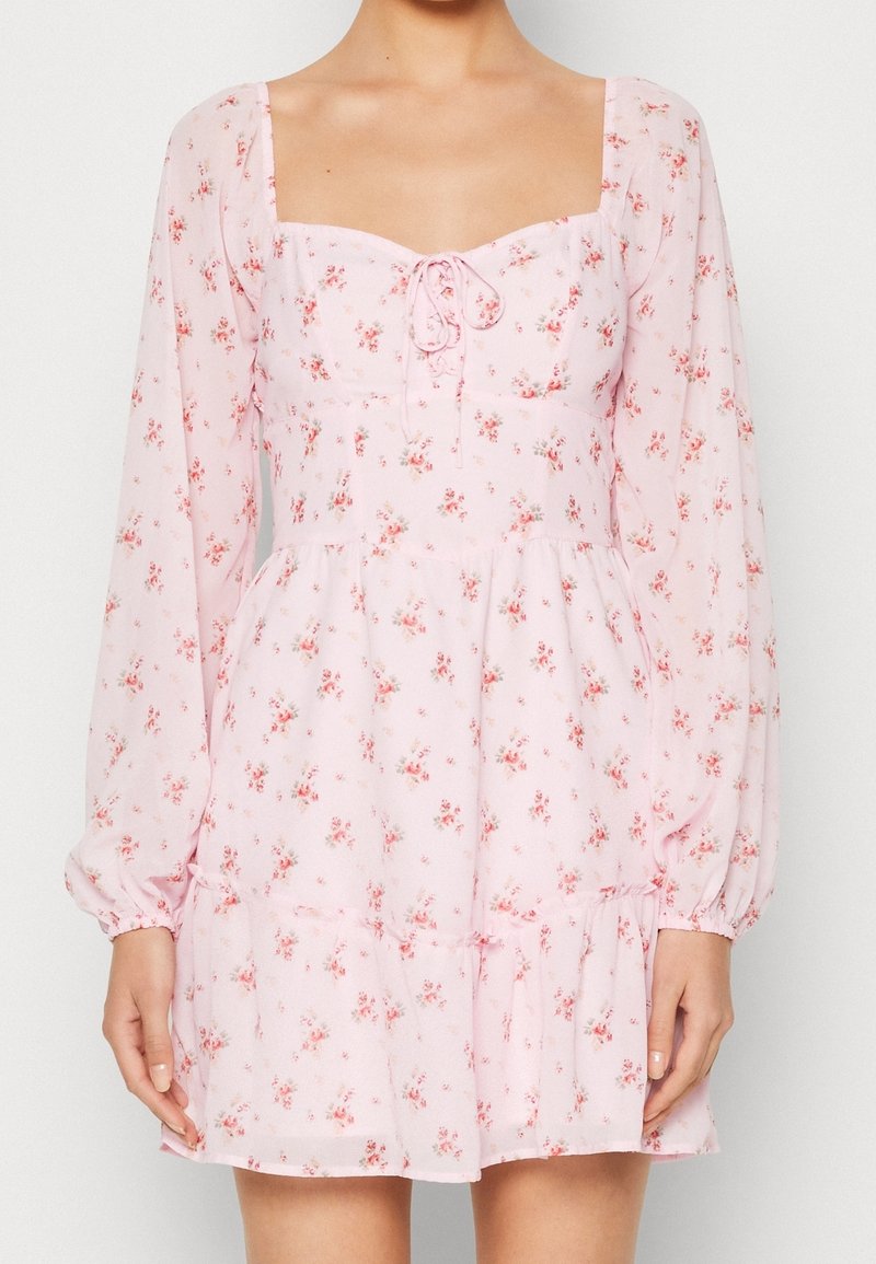 Vestido floral rosa con mangas largas, escote cuadrado, detalle de cordón en el pecho y dobladillo con volantes. Hecho de un tejido liviano y transparente.