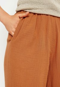 Rdzawoczerwone, lekkie, teksturowane spodnie z elastycznym paskiem w talii i bocznymi kieszeniami, w połączeniu z dzianinowym, jasnym topem.