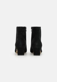 Botas de tobillo de ante negro con tacón cuadrado, que presentan una textura suave y detalles de cremallera lateral. El diseño es sencillo y elegante.