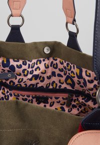 Canvas tote bag with green exterior, pink leopard print lining, navy leather straps and accents, and a zippered pocket inside.