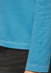 Langärmliges, hellblaues T-Shirt aus weicher Baumwolle, mit rundem Halsausschnitt und genähtem Saum, kombiniert mit schwarzen strukturierten Hosen.