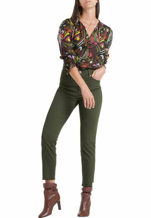 Blouse à motifs floraux avec des manches longues, superposée sur un jean taille haute olive. Bottines marron avec un détail froncé en haut.