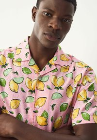 Camisa de manga corta con fondo rosa, que presenta un estampado de limones y limas; hecha de una tela ligera con un corte relajado y cierre de botones.