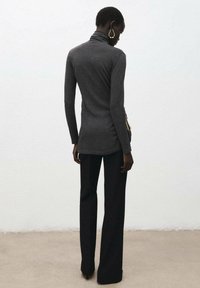 Top de cuello alto gris de manga larga con una silueta ajustada, combinado con pantalones negros acampanados. La tela parece suave y lisa. Pendientes de aro dorados.