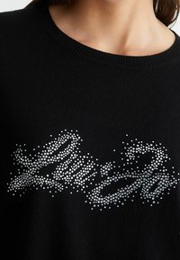 Maglione nero con scollo rotondo e un motivo decorativo di strass argentati in un design astratto sulla parte anteriore.