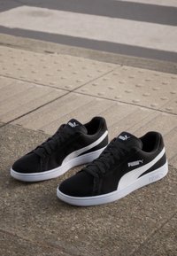 Black sneakers with a smooth leather upper, white accents, and a textured sole; features the Puma logo on the side and tongue.