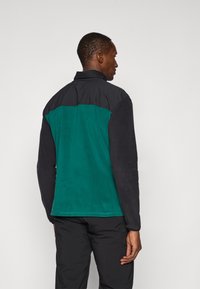Chaqueta negra y verde azulado con cuello, que presenta una parte trasera texturizada en verde azulado, mangas negras lisas y un diseño de corte recto.