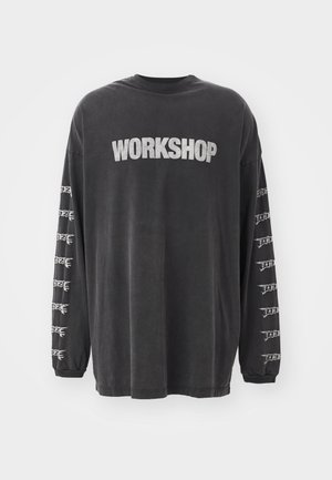 Camiseta de manga larga negra hecha de algodón suave, con la palabra "WORKSHOP" impresa en plata en el frente y gráficos repetidos en las mangas.