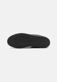 Sort sneakersål med tekstureret design, der har hævede bogstaver med mærkenavnet. Materialet ser ud til at være gummi med en glat overflade.