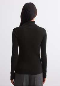 Zwarte geribbelde coltrui, aansluitend ontwerp, lange mouwen, gestructureerde stof, gladde afwerking, gedragen met een grijze rok.