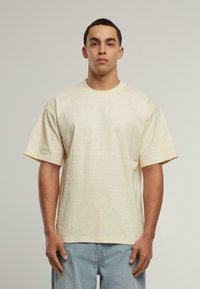 Šviesiai geltonos trumpomis rankovėmis marškinėliai, dekoruoti subtiliu raštu ir mažuoju šviesiu logotipu ant krūtinės. Laisvas kirpimas ir medvilnės medžiaga.