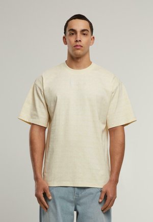 Helles gelbes T-Shirt mit kurzen Ärmeln, das ein dezentes Muster und ein kleines, helles Logo auf der Brust zeigt. Lockere Passform und aus Baumwolle.