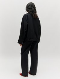 Zwarte oversized sweatshirt met een geribbelde zoom en lange mouwen, gecombineerd met donkere, wijdvallende jeans en rode platte schoenen. Gladde stofstructuur.