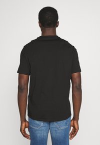 Camiseta negra de manga corta con cuello redondo, hecha de algodón, con una textura suave y un ajuste flexible. Costuras visibles en las mangas.