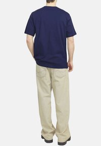 T-shirt court bleu marine à manches courtes avec col rond, associé à un pantalon beige clair à coupe décontractée et des chaussures noires, vu de dos.