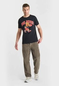 Camiseta negra con un gráfico de un oso y el texto "BIG BOSS"; pantalones de pana caqui con un acabado texturizado; zapatillas deportivas blancas y grises.