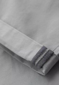 Tissu gris avec une texture lisse, plié. L'ourlet présente un accent gris foncé avec une finition texturée et un détail de couture.