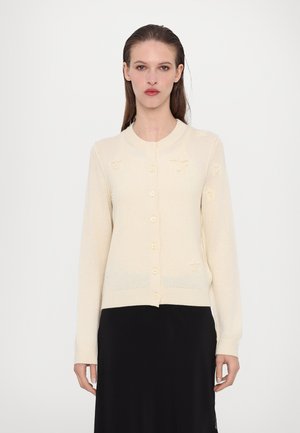 Ljust beige cardigan i stickad tyg, med rund halsringning, långa ärmar och framknäppning med stjärnmönster.