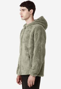 Giacca con cappuccio in pile di verde tenue, con chiusura a zip, tasche laterali e un esterno morbido e testurizzato. Design unisex con una vestibilità rilassata.