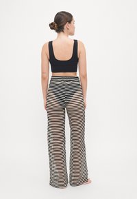 Top corto nero abbinato a pantaloni a gamba larga strisciati, trasparenti, in bianco e nero con un motivo a zigzag. Design leggero, dalla vestibilità casual e con texture.