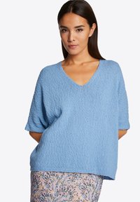 Hellblaue, strukturierte Strickjacke mit V-Ausschnitt und kurzen Ärmeln, kombiniert mit einem Rock mit Blumenmuster. Einfaches, entspannendes Design.