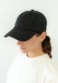 Fekete pamut baseball sapka ívelt karimával; hat panelből és felső gombból áll. A modellen egy krémszínű póló van, amelyen a könnyű szövet textúrája látható.