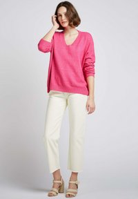 Pull en V rose, coupe ample avec des poignets et un ourlet côtelés, associé à un pantalon large cropped crème et des talons à bride beige.