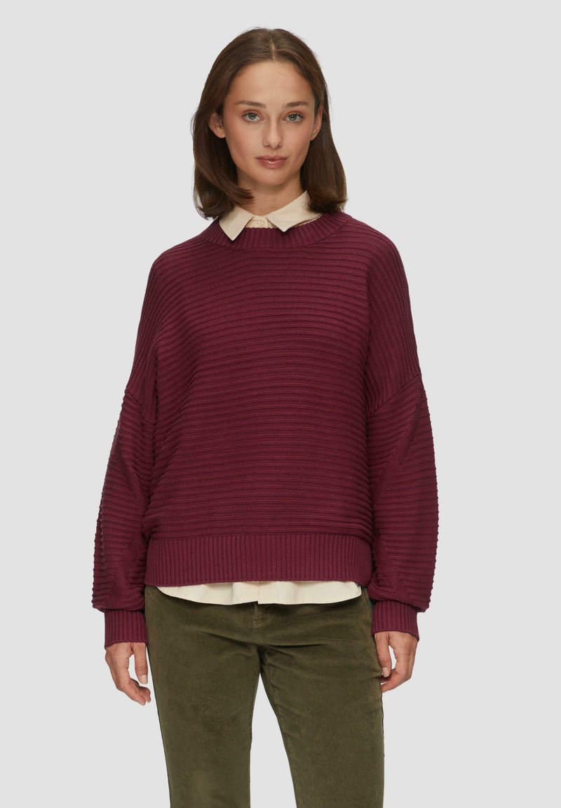 Pull en ribbed bordeaux avec épaules tombantes et un large col, superposé sur une chemise légère à col. Tissu texturé, coupe décontractée.