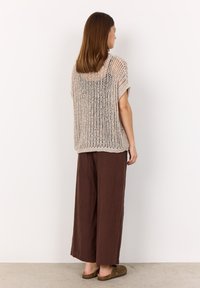 Beige, open-knit sweater with short sleeves, paired with loose, dark brown trousers, and brown slip-on shoes. Minimalist design and relaxed fit.