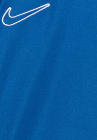 Tela azul con una textura suave que presenta un logo de Nike bordado en blanco en la parte superior izquierda.