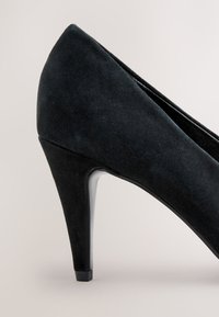 Czarny zamszowy but na wysokim obcasie z ostrym noskiem, charakteryzujący się eleganckim designem i gładkim, błyszczącym obcasem dla dodatkowego kontrastu.