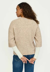 Beige, pehmeast kudumist suvekleit, lühikeste varrukatega, lõdva siluettiga. Kombineeritud heledat tooni pika varrukaga pluusi ja tumehallide teksadega.