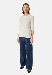 Ljusgrå stickad tröja med ribbad textur, korta ärmar, i kombination med mörkblå vida jeans och svarta spetsiga skor.