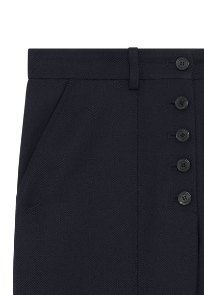 Nahaufnahme eines dunkelblauen Rocks mit seitlichen Taschen, Gürtelschlaufen und fünf vertikal auf der rechten Seite angeordneten schwarzen Knöpfen.