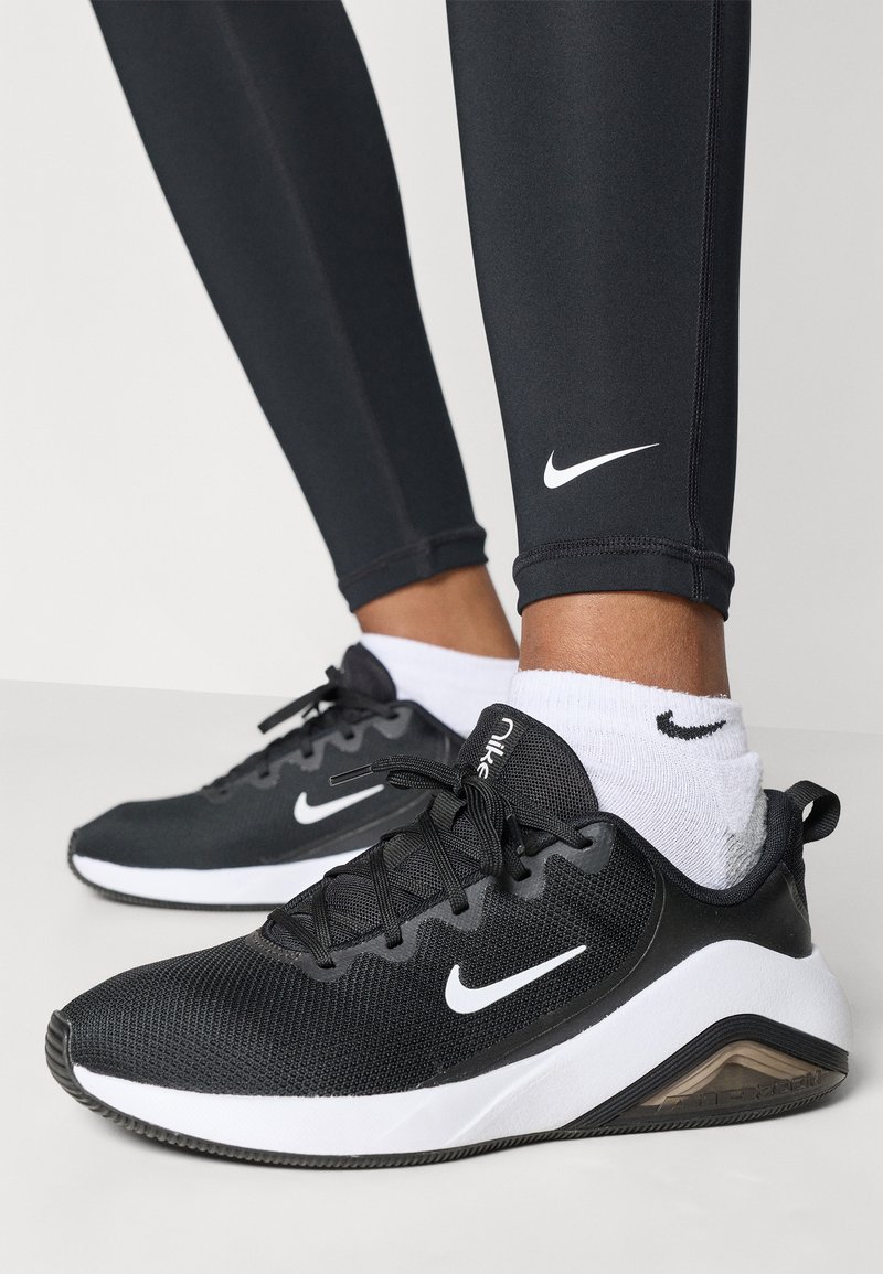 Black athletic shoes with a mesh upper, white accents, and rubber sole. Tall black leggings and white Nike socks visible.