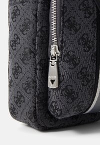 Bolsa de tela negra con un sutil patrón de monograma, acentuada con una cremallera plateada y un tirador triangular. Superficie texturizada con una forma estructurada.