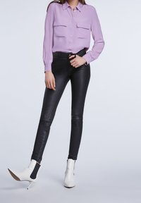Camicia lunga manica di un viola chiaro con due tasche sul petto, abbinata a pantaloni in pelle nera aderenti e stivaletti bianchi con tacco alto.