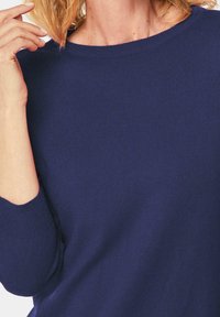 Dunkelblauer gestrickter Pullover mit weitem Ausschnitt, gerippten Bündchen und einer weichen Textur, die auf den Ausschnitt- und Schulterbereich fokussiert.