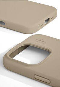 Coque de smartphone beige avec finition mate, bords arrondis et découpes pour la caméra et les ports. Présente un logo en relief "IDEAL OF SWEDEN".