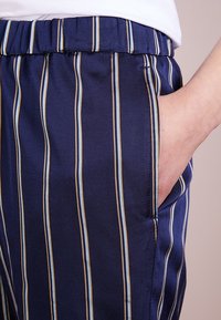 Navy pruhované kalhoty vyrobené z texturované látky, s vertikálními pruhy v světle modré a zlaté barvě, mají boční kapsu a elastický pas.